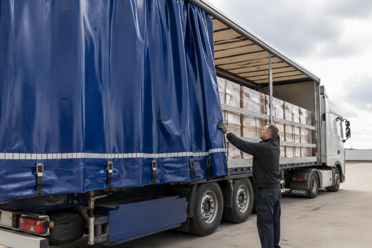 A driver operating a sliding PVC curtain side on a long-haul delivery truck